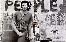 Withers smiling and leaning in front of a brick wall