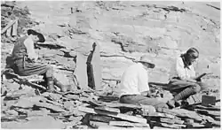 Photo of two men and a woman digging among rocks.