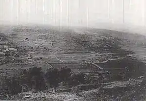 Landscape photo taken from high hill shows two villages and fields with a road crossing in the middle distance from left to right of the photo.