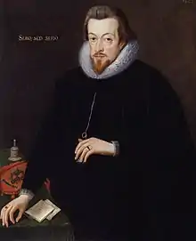 A portrait of Robert Cecil, who is standing at a table wearing black robes. He has neck-length brown hair and a pointed goatee. He has gold lettering behind him, which reads "sero, sed serio".