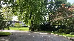 The former site of the Roslyn–Flower Hill Elementary School in 2020, as viewed from Center Drive.  The land was sold and developed for single-family homes. Note part of the school's old fence and the faded school district sign on it behind the bushes at right.