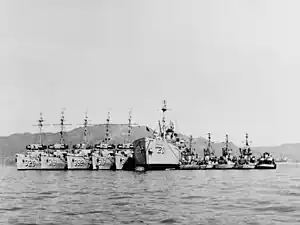 USS Laertes (AR-20) is flanked by five minesweepers and five motor minesweepers at Sasebo, Japan, in 1952. USS Curlew (AMS-8) is the middle ship of the group on the right.